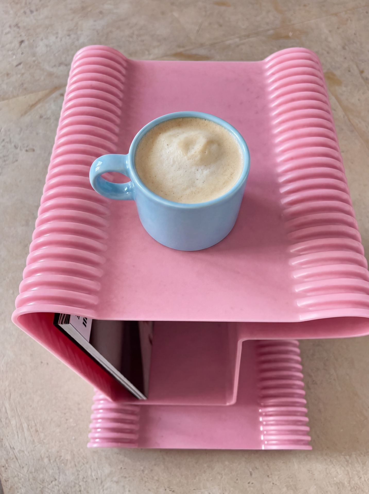 A blue coffee mug on a pink sculptural side table.